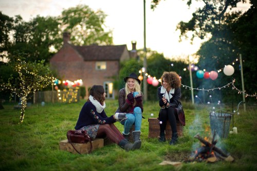 Models (L-R) Lizzie Bowden, Sophie Harries and Leanne Pollock relax by a bonfire. New Look behind the scenes shoot of their Autumn / Winter 2013 collection advertising film by Cherry Duck. Walnuts Farm, Old Heathfield, East Sussex, UK. August 22, 2013. Photo: ©Edmond Terakopian