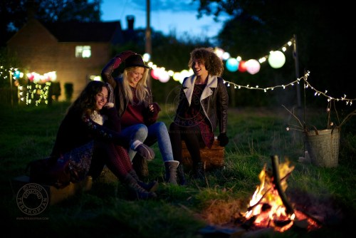 Models (L-R) Lizzie Bowden, Sophie Harries and Leanne Pollock relax by a bonfire. New Look behind the scenes shoot of their Autumn / Winter 2013 collection advertising film by Cherry Duck. Walnuts Farm, Old Heathfield, East Sussex, UK. August 22, 2013. Photo: ©Edmond Terakopian